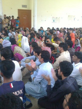 Karachi University students and faculty crowd the lobby outside the Arts Auditorium, locked by the administration